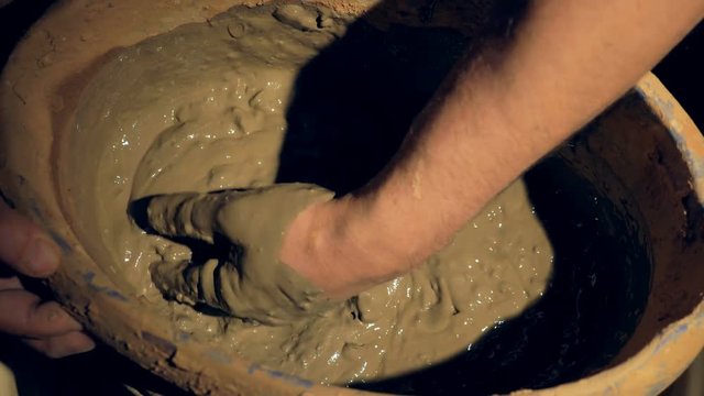 Male hands mix clay and break down large lumps. 