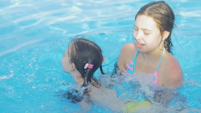 Beautiful young girl teaches her little sister to swim in the pool