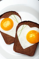 Two toast with scrambled eggs in the shape of a heart on a white plate .On dark stone background.Inscription love of red satin ribbon.Creative Valentine day background.Love concept.closeup.Breakfast