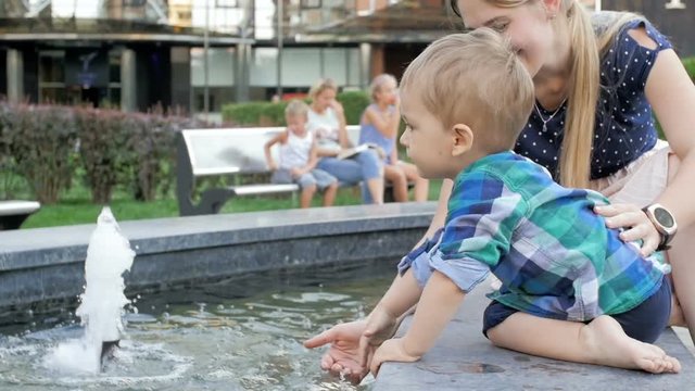 Slow motion video of cute toddler boy with mother playing with fountain at park