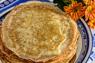 Freshly baked pancakes, a teapot, a glass with tea, sour cream are on a table set for the maslenitsa, pancake week celebration