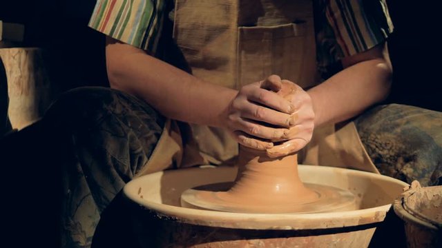 Potters hands reshape a tall tower of clay into a shallow pot. 