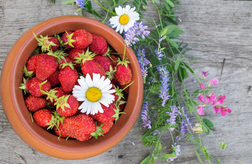 Ripe strawberries in ceramic bows and flowers on a wooden bench