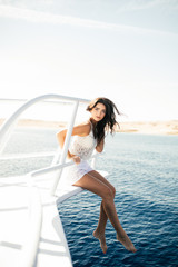 Beautiful young woman standing on the nose of the yacht with legs on water at a sunny summer day