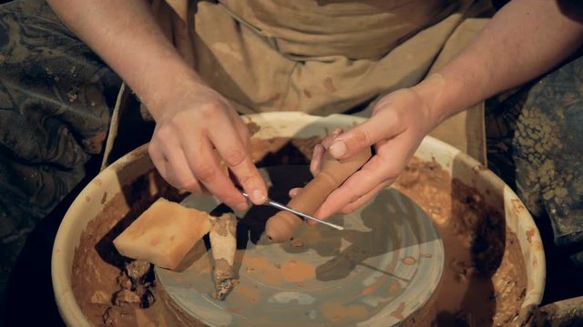 A potter uses a cleaning tool on a greenware handle.  