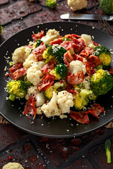 Steamed Broccoli, Cauliflower Salad with Bacon, parmesan cheese in a black plate. healthy food concept