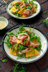 Fresh Tasty Persimmon salad with arugula, parma ham, olive oil and herbs. autumn, winter healthy food