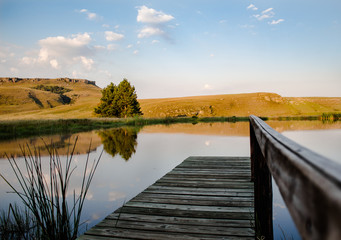 Small pond with focused hills in the background and a soft focus pier foreground with a rail leading into the hard focus center.