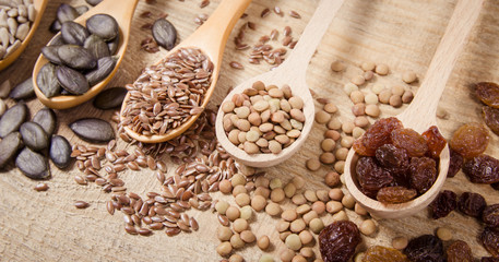 Flaxseed, pumpkin, raisins, lentils and sunflower seeds in wooden spoons.