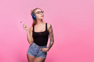 Sexy hot woman listening to music and having a lollipop. Pink background in studio photo