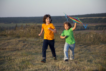 Children playing kite on summer sunset meadow