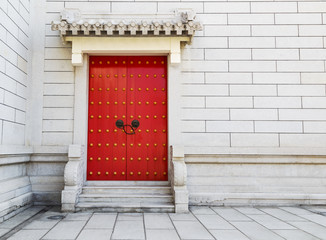 Red Chinese door with locked key and bronze lion head knob on concrete wall