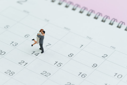 Valentines day reminder with lovely miniature couple standing on 14 Feb calendar on pink background