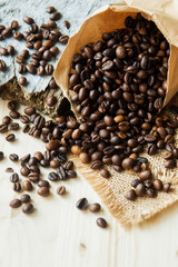 Roasted coffee beans scattered from paper bag over dark gray granite plate, captured from top view with sharp focus