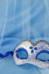 Image of delicate elegant venetian mask over blue silk and tulle fabric background.