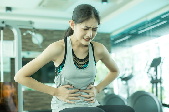 Woman touching her stomach with hands while exercise. Young asian woman feel pain in her stomach.