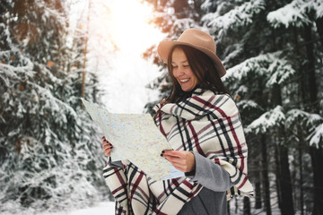 Happy and smiling traveling woman in scarf and hat hold map in hand among snowy trees in winter forest © leonidkos