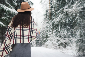 Pretty female hipster walking among winter forest and hold map in hand. Wearing scarf and hat