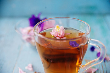Cup of tea and branch of small pink roses on rustic table.