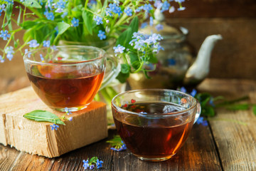 Tea cup, teapot, honey jar and summer bouquet of blue cornflowers on table outdoors. Summer still life.