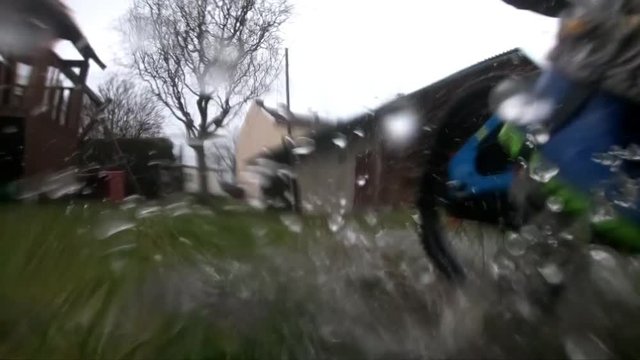 The boy enjoys a good ride. Driving through puddles on a bicycle. Slow motion.