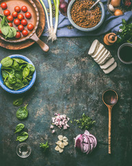 Vegetarian food cooking background. Spinach,tomatoes, lentil and fresh seasoning with cooking spoon on rustic kitchen table background, top view, frame. Clean food and healthy eating concept