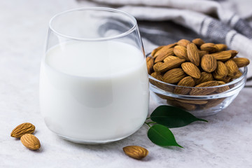 Healthy vegan almond milk in a glass and almonds on white marble background. Selective focus, space for text.