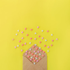 Multicolor sweets sugar candy hearts fly out of craft paper envelope on the bright yellow background . Valentine day. love concept. Gift, message for lover. Space for text. Square card