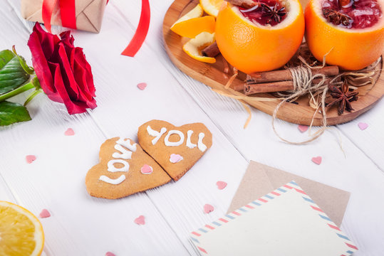 Festive composition with cookies in shape of heart with Love you words, rose, unusual served in orange mulled wine on the white table. Valentine' s day surprize for lover. Selective focus.