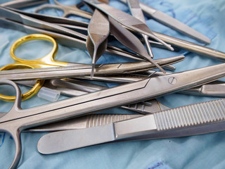Close-up detail of a pile of surgical instruments, including metzenbaum and mayo scissors, adson...