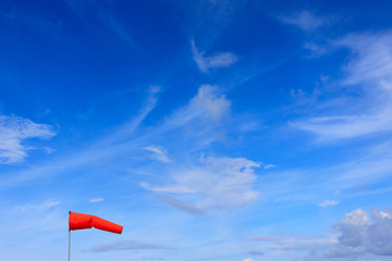 Orange wind sock in blue sky and white cloud background.