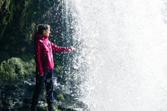 Feamale hiker, tourist, model touching water under the Sgwd Yr Eira Waterfall in Wales