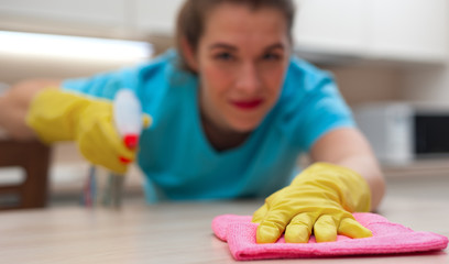 Blurred beautiful young woman housewife wipes furniture with rag and spray in rubber gloves on her hands. Focus on rag