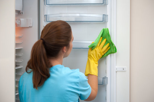 Charming young woman housewife in rubber gloves - wipes kitchen fridge. Cleaning the kitchen