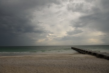 Deserted sandy beach and concrete pier under cloudy and stormy skies