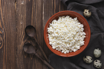 Cottage cheese in a ceramic bowl, quail eggs, wooden spoons and napkin on a wooden background. Top view.
