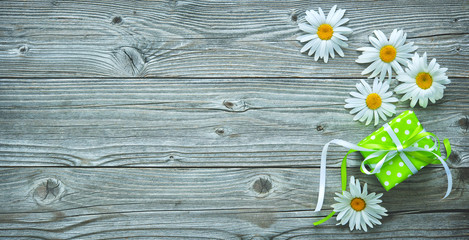 Gift box and daisy flowers on old wooden planks