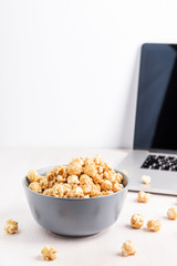 Bowl with popcorn and laptop. Sweet caramel popcorn on white background.  Movie on computer at home