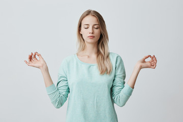Restful peaceful blonde female feels relaxed, stands in lotus pose, tries to concentrate or to be...
