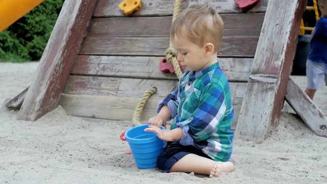 Slow motion video of cute toddler boy digging hole in sandbox on playground at park