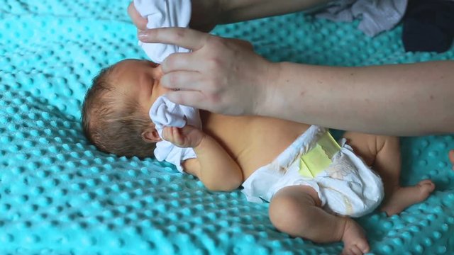 Mother dressing her newborn baby while lying on bed
