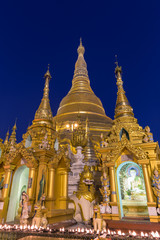 Fototapeta premium Two small pagodas and many statues in front of the gilded Shwedagon Pagoda in Yangon, Myanmar in the evening.