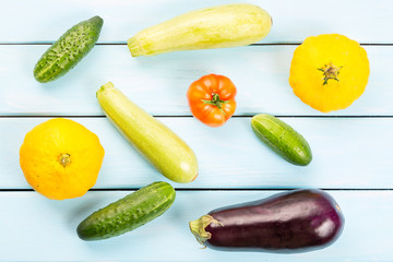 Vegetarian healthy food with vegetables. Tomato, cucumbers, bush pumpkins, eggplants and marrows on blue wooden table.