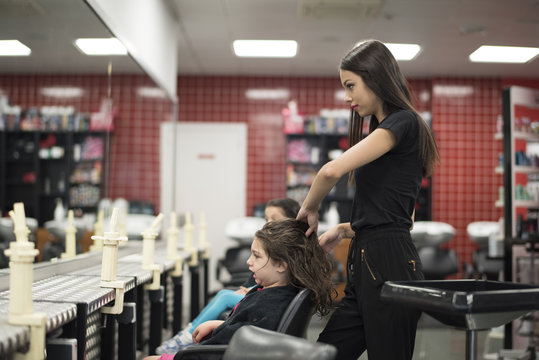 Young hairdresser cutting little girl hair in beauty center schol