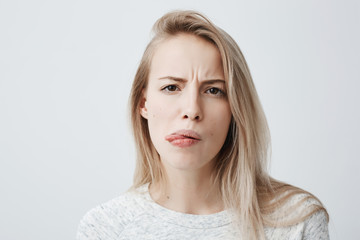 Naklejka premium Negative human reaction, feelings and attitude. Close-up portrait of disgusted squeamish blonde woman in casual wear grimacing, sticking out tongue, feeling nauseous because of bad smell or stink