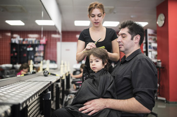 Fototapeta na wymiar Hairdresser cuts little baby hair with fathers help