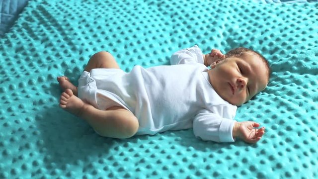 Adorable newborn baby wearing white rompers and lying on blue blanket
