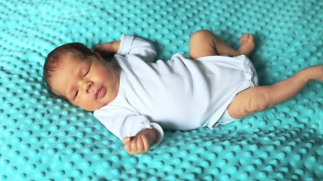 Adorable newborn baby lying on blue blanket and yawning
