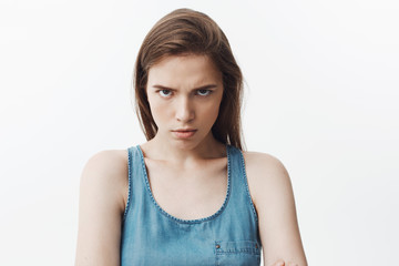 Close up of agressive attractive young caucasian woman with dark long hair in blue shirt looking in camera with angry face expression, being mad after husbend come home drunk with lipstick on his neck