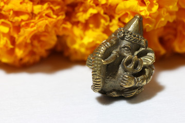 Mini Ganesha made from brass with yellow marigold flower and white background, the son of Uma Devi...